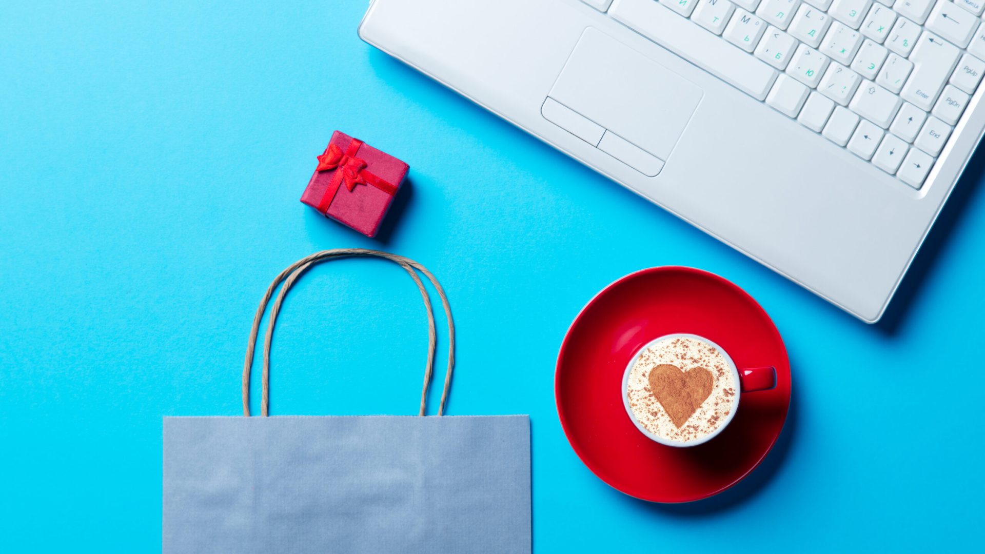 cup of coffee, blue shopping bag, gift and laptop on the blue background