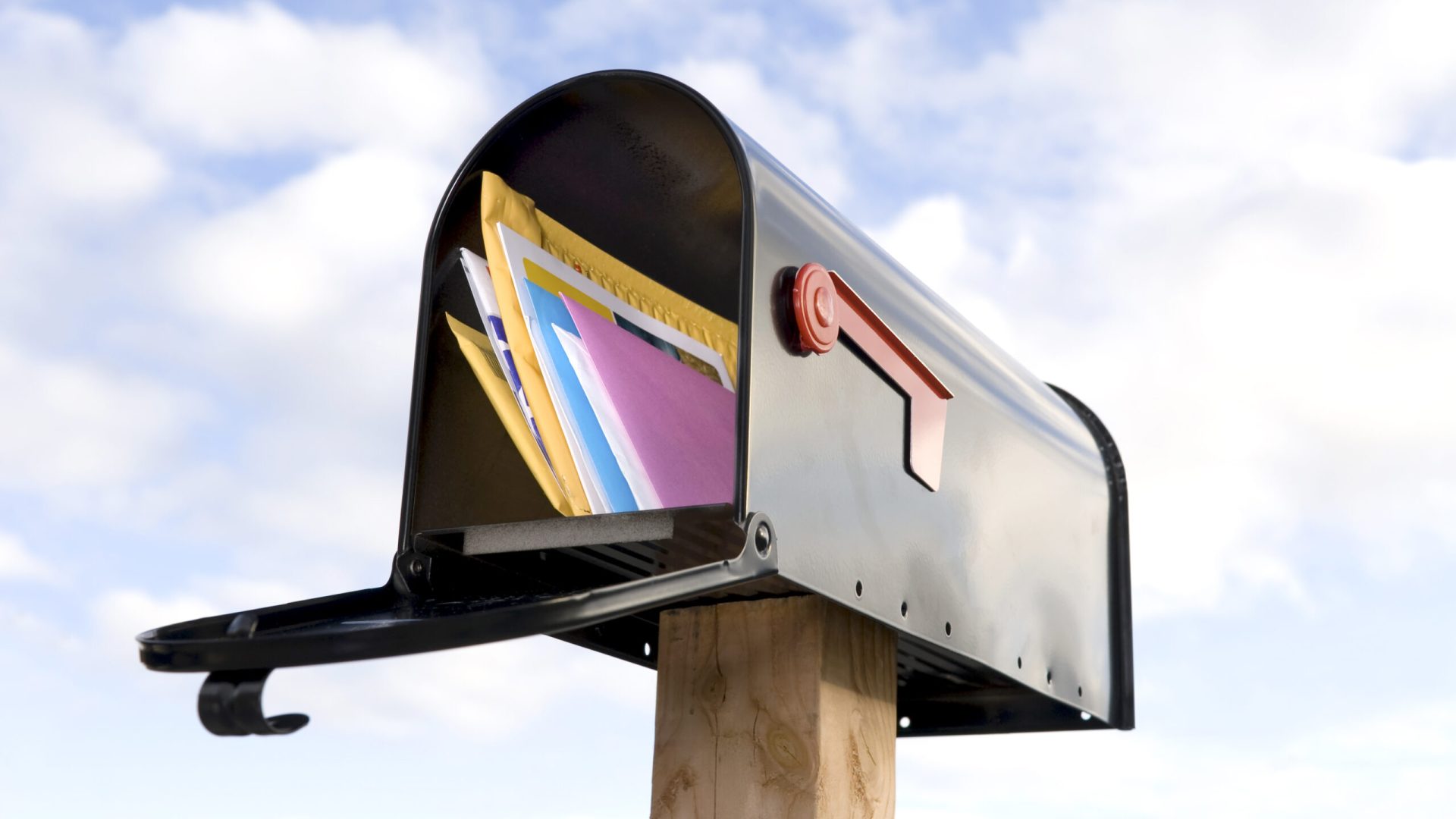 A mailbox full of mail against a blue and puffy white cloud sky